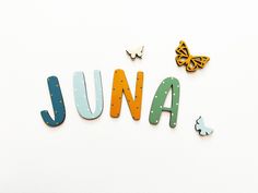 the word june spelled with wooden letters and butterflies on a white background, surrounded by other colorful objects