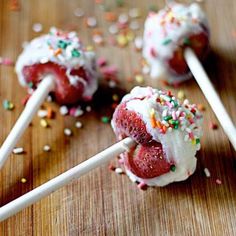 some cake pops with sprinkles and white frosting on them sitting on a wooden table