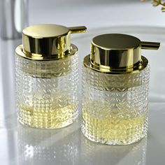 two clear glass jars with gold lids on a white counter next to a silver faucet