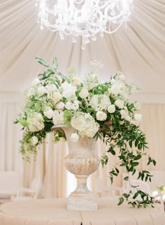 a vase filled with white flowers sitting on top of a wooden table next to a chandelier