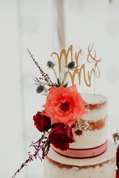 a wedding cake with red flowers and mr and mrs topper on the bottom tier