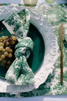 a green plate with grapes and napkins on it next to a fork and knife