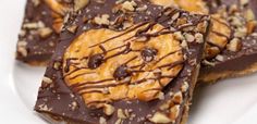 four pieces of chocolate peanut butter pretzel bars on a white plate with nuts