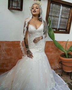 a woman in a wedding dress standing next to a potted plant and wearing a veil