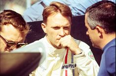 a man sitting on top of a bench next to another man in a race suit