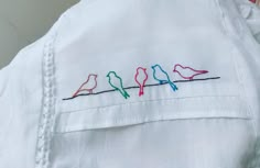 a white shirt with three birds embroidered on the chest and two different colored stitches across the chest