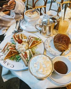 a table topped with plates filled with sandwiches and cups of coffee next to each other