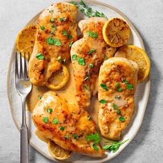 a plate with chicken, lemons and parsley garnish on it next to a fork