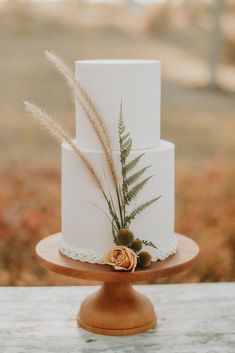 a three tiered white wedding cake with greenery on top