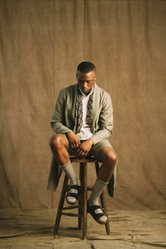 a man sitting on top of a wooden chair in front of a brown wall wearing socks