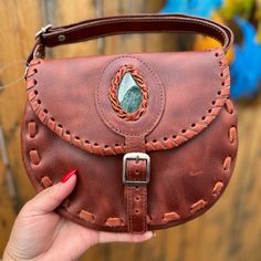 a hand holding a brown leather purse with a stone in it