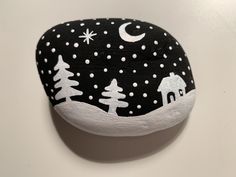 a black and white painted rock with trees and houses in the snow at night time