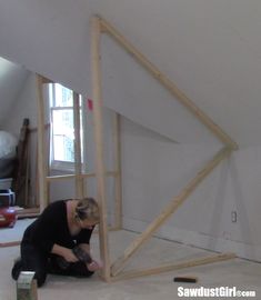 a woman kneeling down on the floor in front of a wooden frame that is being built