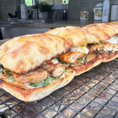 two sandwiches sitting on top of a metal rack next to an oven filled with food