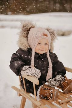 a small child is sitting on a sled in the snow wearing a hat and mittens