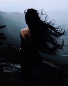 a woman with long hair standing on top of a hill