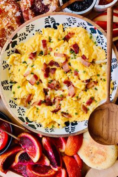 a bowl filled with eggs and bacon next to sliced fruit