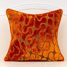 an orange and gold pillow on a white chair with the back turned to the side