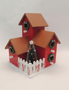 a red house with a christmas tree and wreath on the roof is shown in front of a white picket fence