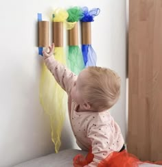 a baby playing with some toilet paper rolls on the wall next to it's head