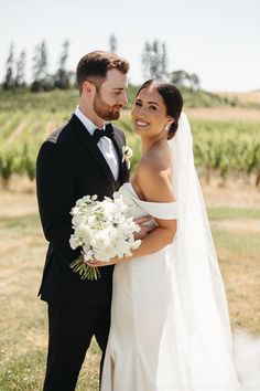 a bride and groom pose for a photo in front of the vineyard at their wedding