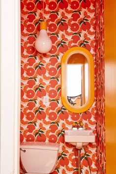 a bathroom with orange and white wallpaper has a mirror, sink, and toilet