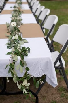 a long table with white flowers and greenery is set up for an outdoor event