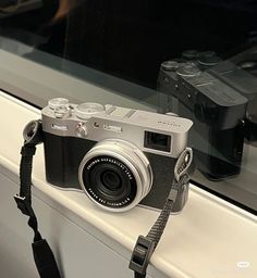 a silver camera sitting on top of a window sill next to a black camera