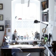 a man sitting at a desk in front of a window with lots of clutter