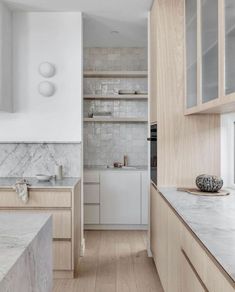 a white kitchen with marble counter tops and wooden cabinets, along with an island in the middle