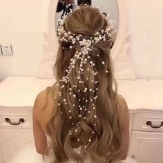 a woman with long hair and pearls on her head sitting in front of a mirror