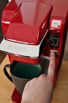 a person is pressing the button on a red coffee maker