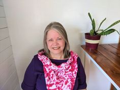 a woman sitting in front of a wooden table with a potted plant behind her