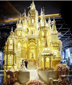 a couple standing in front of a golden castle with roses on the ground and flowers all around it