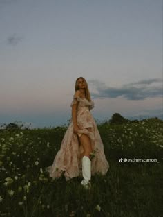 a woman in a dress and boots is standing in the middle of a field with flowers