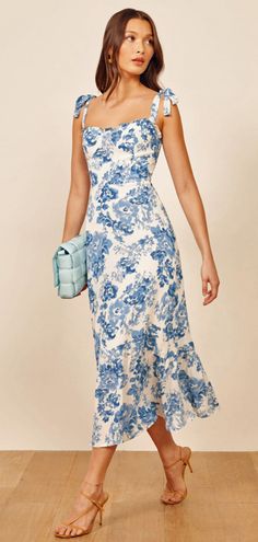 a woman in a blue and white dress standing on a wooden floor with her handbag