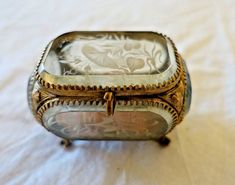 an antique silver box sitting on top of a white cloth covered table with a flowered design