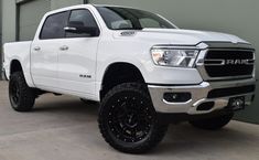 a white ram truck parked in front of a garage door with black wheels and tires