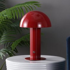 a red lamp sitting on top of a white table next to a blue chair and potted plant