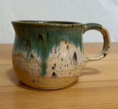 a green and brown cup sitting on top of a wooden table next to a white wall