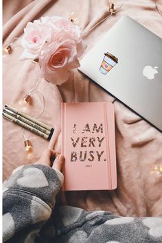 a pink notebook with the words i am very busy written on it next to an apple laptop