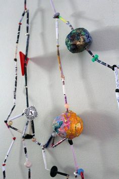 an art piece made out of beads and other items hanging on the wall with one bead dangling from it's end