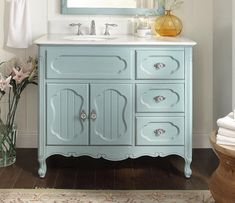 a bathroom vanity with blue painted drawers and mirror above it, along with flowers in a vase