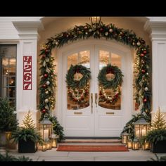 two christmas wreaths on the front door of a house with lit candles and lanterns