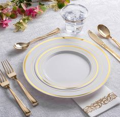 a white and gold place setting with silverware, napkins, and flowers in the background