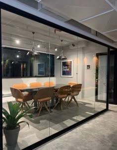 a glass walled conference room with wooden chairs and table in the center, surrounded by potted plants