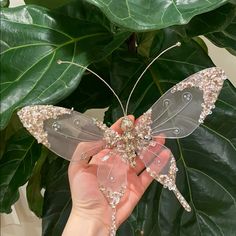 a hand holding a glass butterfly on top of a green plant