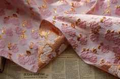 pink and gold floral fabric laying on top of an old newspaper