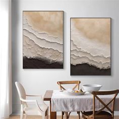 two paintings hanging on the wall above a dining room table with chairs and a white table cloth