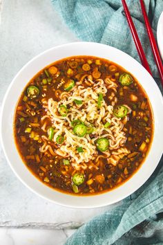 a bowl of soup with noodles, vegetables and meat on a blue towel next to chopsticks